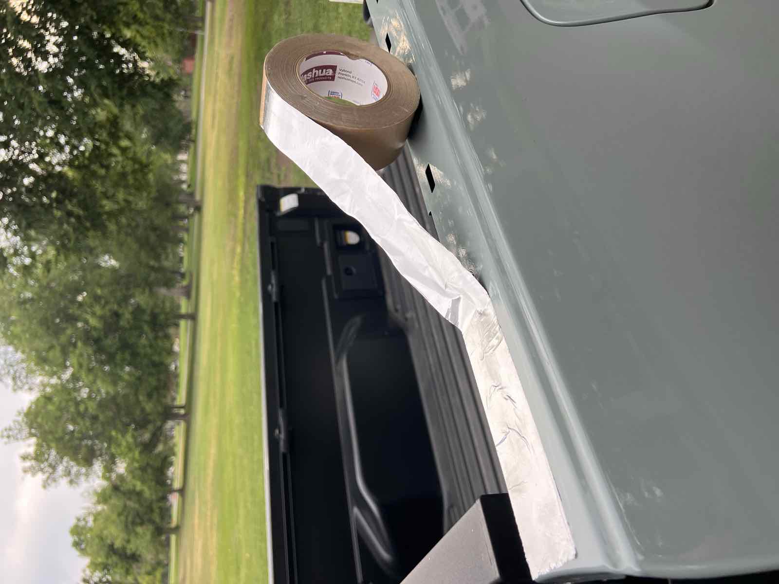 A strip of Nashua aluminum foil tape applied along the top of a Tacoma bed rail covering the open holes, with the roll of tape resting on the rail.