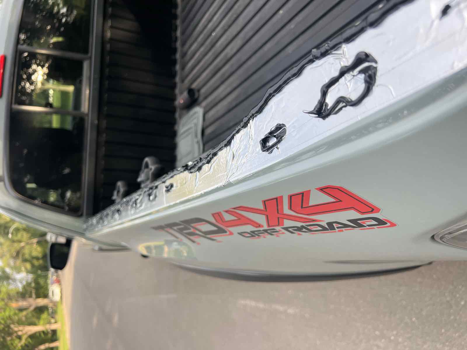 A bead of black Sikaflex 221 run along the inner bed rail and around each hole over the foil tape, on a 2023 Tacoma with a TRD 4x4 Off-Road decal on the bedside.
