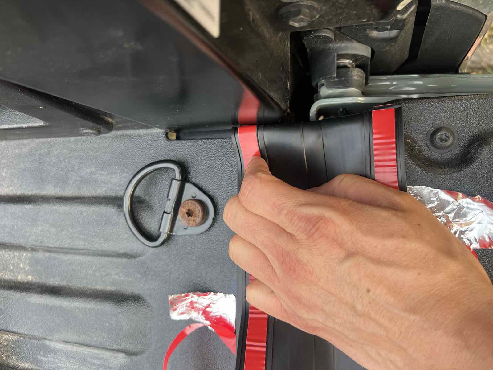 The end of a ROK Block seal folded downward at the right side of a Tacoma tailgate to mark where it needs to be cut and trimmed to length.